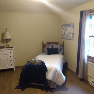 A cozy bedroom with a single bed, white dresser, and window.