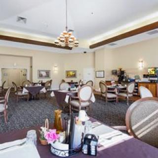 An elegant dining room with neatly arranged tables and chairs, featuring a chandelier and warm decor.