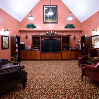 A traditional living room featuring a large entertainment center with surrounding bookshelves and comfortable armchairs on patterned carpet.