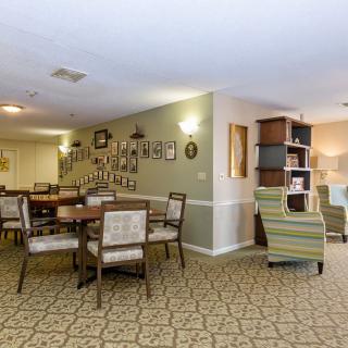 A cozy living and dining area with chairs, tables, and wall decorations on a carpeted floor.