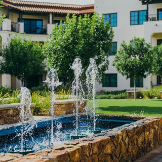 A serene courtyard featuring a bubbling fountain surrounded by lush greenery and residential buildings.
