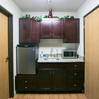 A compact kitchen setup with dark wood cabinets, a small refrigerator, a microwave, and a sink.