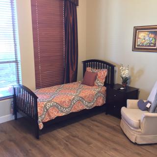 A cozy bedroom featuring a single bed with colorful bedding, a nightstand with decor items, and a comfortable chair.