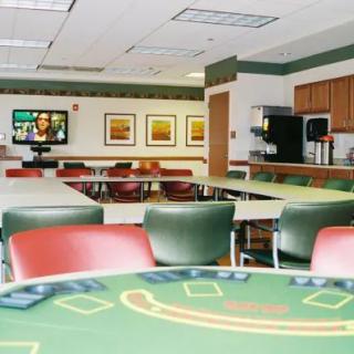 An empty casino-style game room with green felt tables and red chairs.