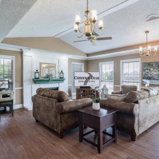 A spacious and elegantly designed living room featuring comfortable sofas, a chandelier, and large windows allowing natural light.