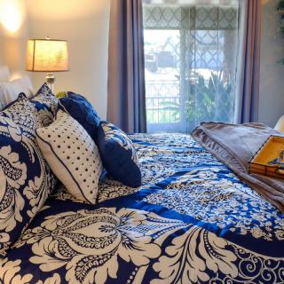 A beautifully decorated bedroom with patterned bedding and multiple pillows, softly lit by a bedside lamp.