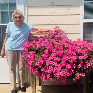 A woman stands beside a vibrant display of pink flowers on a sunny day.