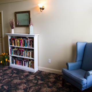 A cozy living room corner featuring a blue armchair and a small bookshelf filled with books.