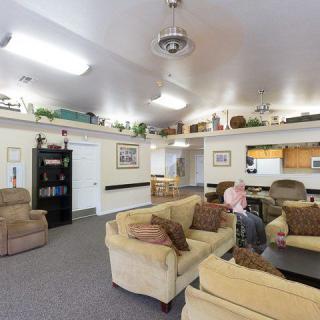 A spacious living room with comfortable seating, decorative plants, and a kitchen in the background.