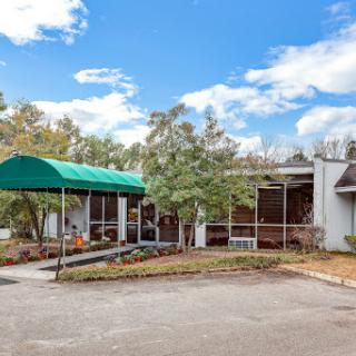 A view of a modern building with a green canopy, surrounded by trees under a bright blue sky.