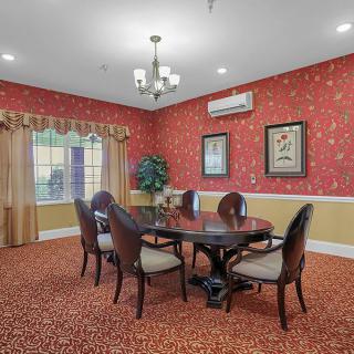 A cozy dining room with patterned wallpaper, featuring a round table and elegant chairs under a chandelier.