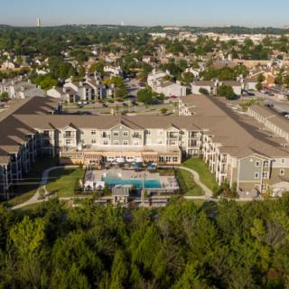 Aerial view of a residential apartment complex with a swimming pool, surrounded by greenery and suburban landscape.