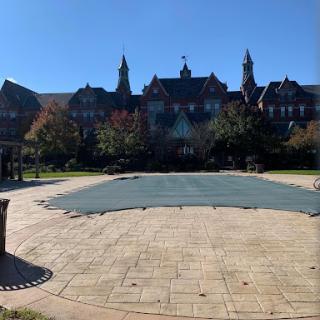 A sunny day at a scenic park featuring a large, covered area in front of an architectural structure.