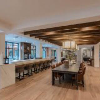 A spacious modern kitchen and dining area featuring a long table, bar stools, and stylish pendant lighting.