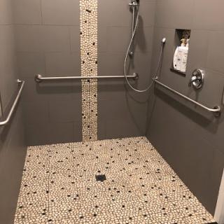 A spacious and modern accessible shower equipped with handrails and a textured tile floor.