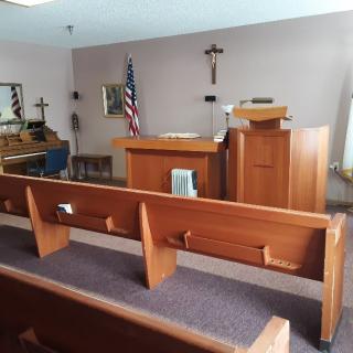 A small chapel with rows of wooden pews, a pulpit, and religious symbols.