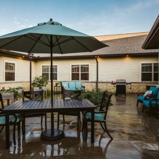 A tranquil patio area featuring outdoor furniture, including a table with an umbrella and chairs, set in a courtyard surrounded by a building exterior.