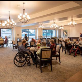 A lively dining room filled with senior residents enjoying a meal together in a community setting.