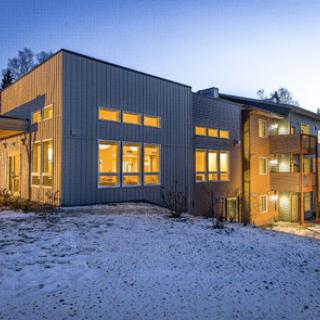 A modern building illuminated during the evening with snow on the ground.