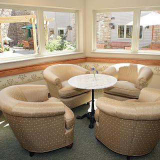 A cozy seating area with four upholstered chairs around a round table, surrounded by windows.