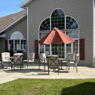 A sunny patio with outdoor furniture and a red umbrella in front of a house.