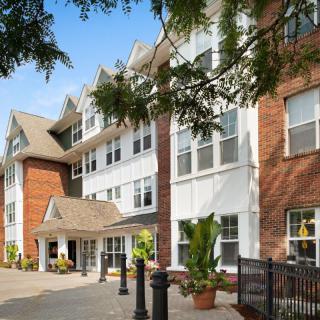 A multi-story residential building with a welcoming entrance, surrounded by trees.