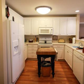 A cozy kitchen with white cabinets, wooden flooring, and a small central island.