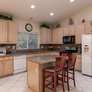 A spacious kitchen with wooden cabinets, a central island with red bar stools, and modern appliances.