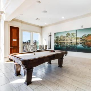 A bright game room featuring a pool table, large windows, and wall art.