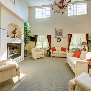 A spacious living room with elegant furnishings, featuring a fireplace, large windows, and a chandelier.