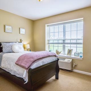 A cozy bedroom with a single bed, large window, and soft lighting.