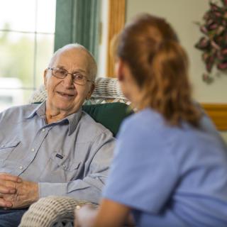 An elderly man having a conversation with a caregiver in a home setting.