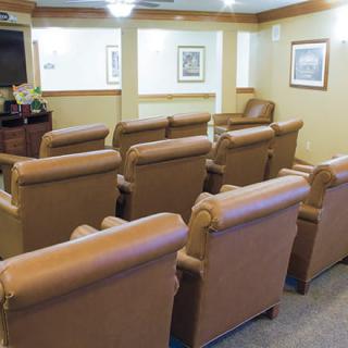 A cozy theater room with rows of comfortable leather chairs facing a large screen.
