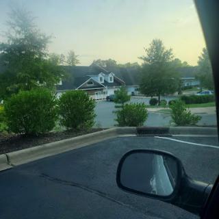 A serene view of a parking lot surrounded by greenery and buildings in the morning.