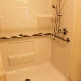 A bathroom shower with accessibility grab bars and a handheld showerhead.