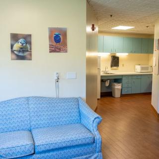 A cozy waiting room with a blue sofa and a kitchenette in the background.
