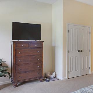 A bedroom with a wooden dresser topped by a television, next to a closed closet door.