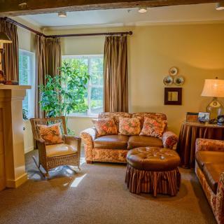 A cozy living room with warm colors, featuring a sofa, armchair, and large windows letting in natural light.