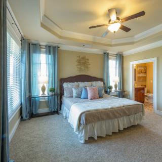 A spacious and well-decorated bedroom with a large bed, ceiling fan, and ample natural light.