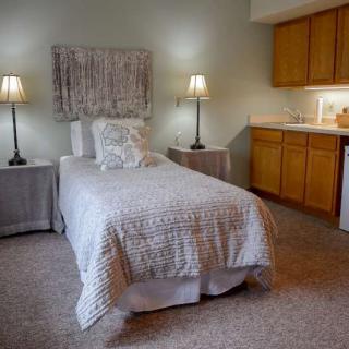 A cozy bedroom featuring a single bed with a neutral color scheme, two lamps on bedside tables, and built-in cabinets.