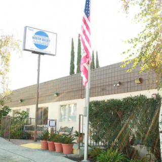 A small building with a sign and an American flag in front, surrounded by plants.