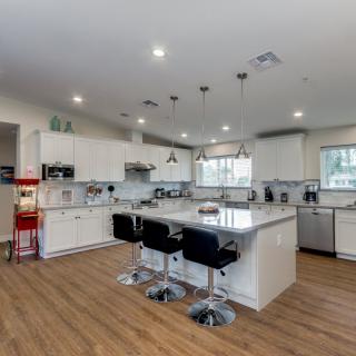 A modern kitchen featuring an island with bar stools, white cabinets, and hardwood flooring.
