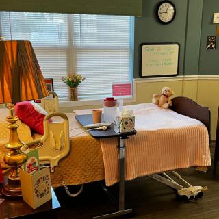 A cozy hospital room with a bed, lamp, and a teddy bear by the window.