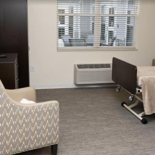 A clean and well-organized hospital room with a bed and a comfortable chair near a window.