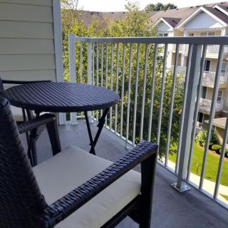 A cozy balcony with a wicker table and chair set overlooking a suburban apartment complex.