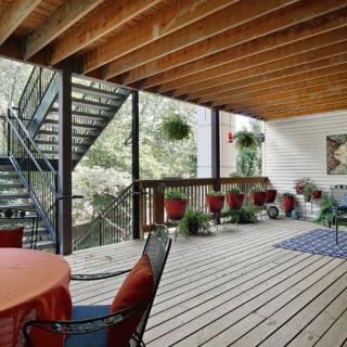A cozy outdoor patio with wooden flooring, decorated with plants and comfortable furniture.