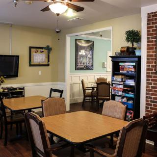A cozy dining area with wooden tables and chairs, featuring a bookshelf and a brick accent wall.