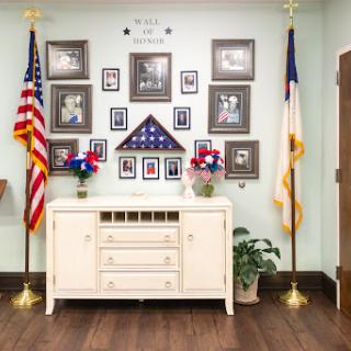 A serene memorial display featuring flags and framed photographs, honoring service members.