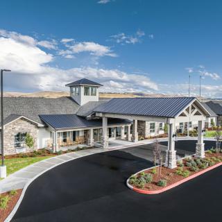 A well-maintained building with a covered entrance and landscaped surroundings under a cloudy blue sky.