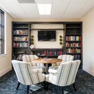 A cozy meeting room with bookshelves, a round table, and comfortable chairs.